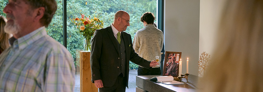 Uitvaartverzorger Peer zet een borrel neer bij de foto van de overledene