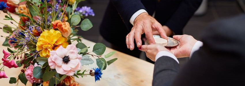 Twee medewerkers van een uitvaartlocatie leggen een crematiesteentje op een kist met bloemstuk